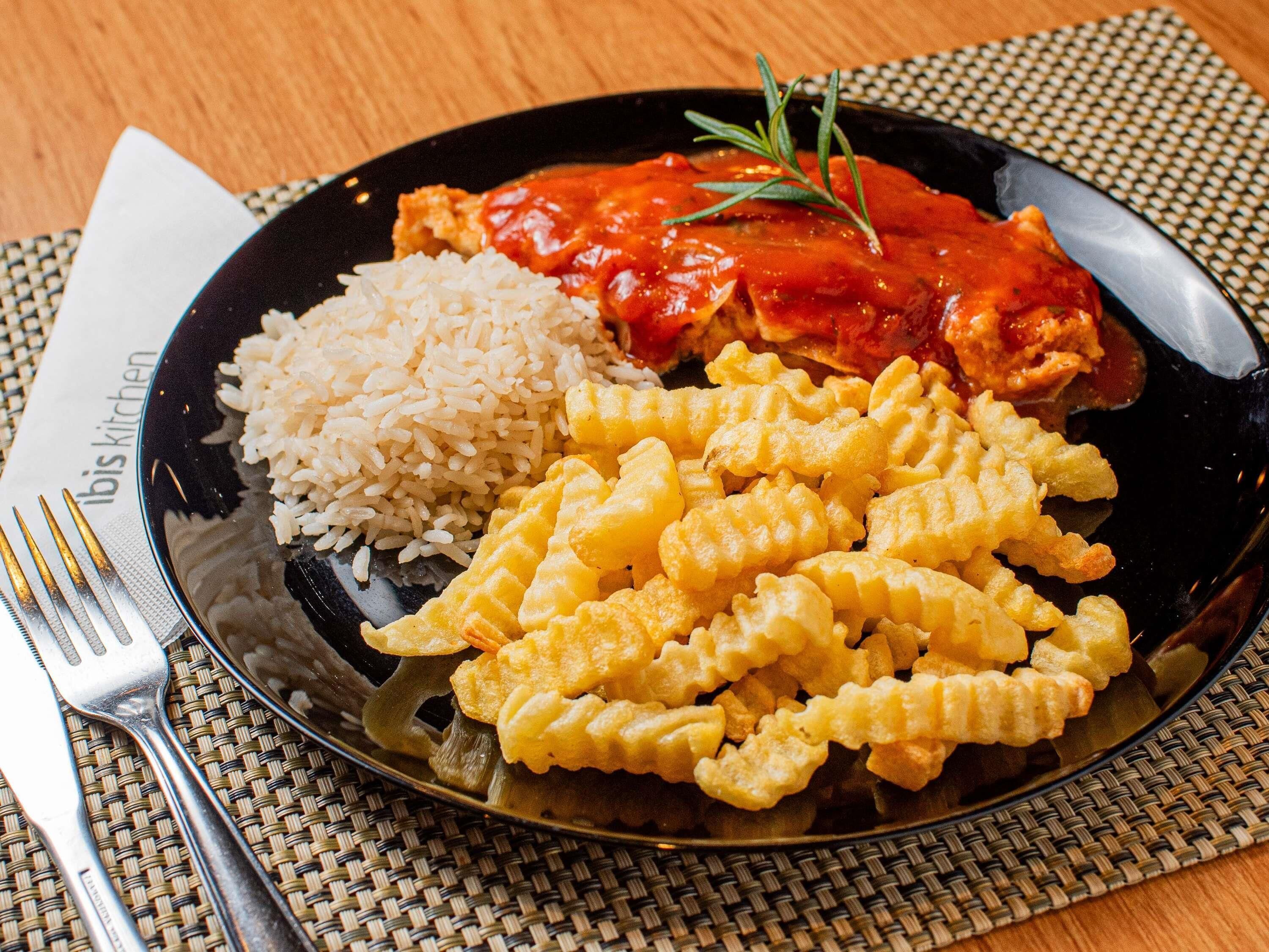 A plate with rice, fried food, and a tomato-based dish, accompanied by cutlery and a placemat.