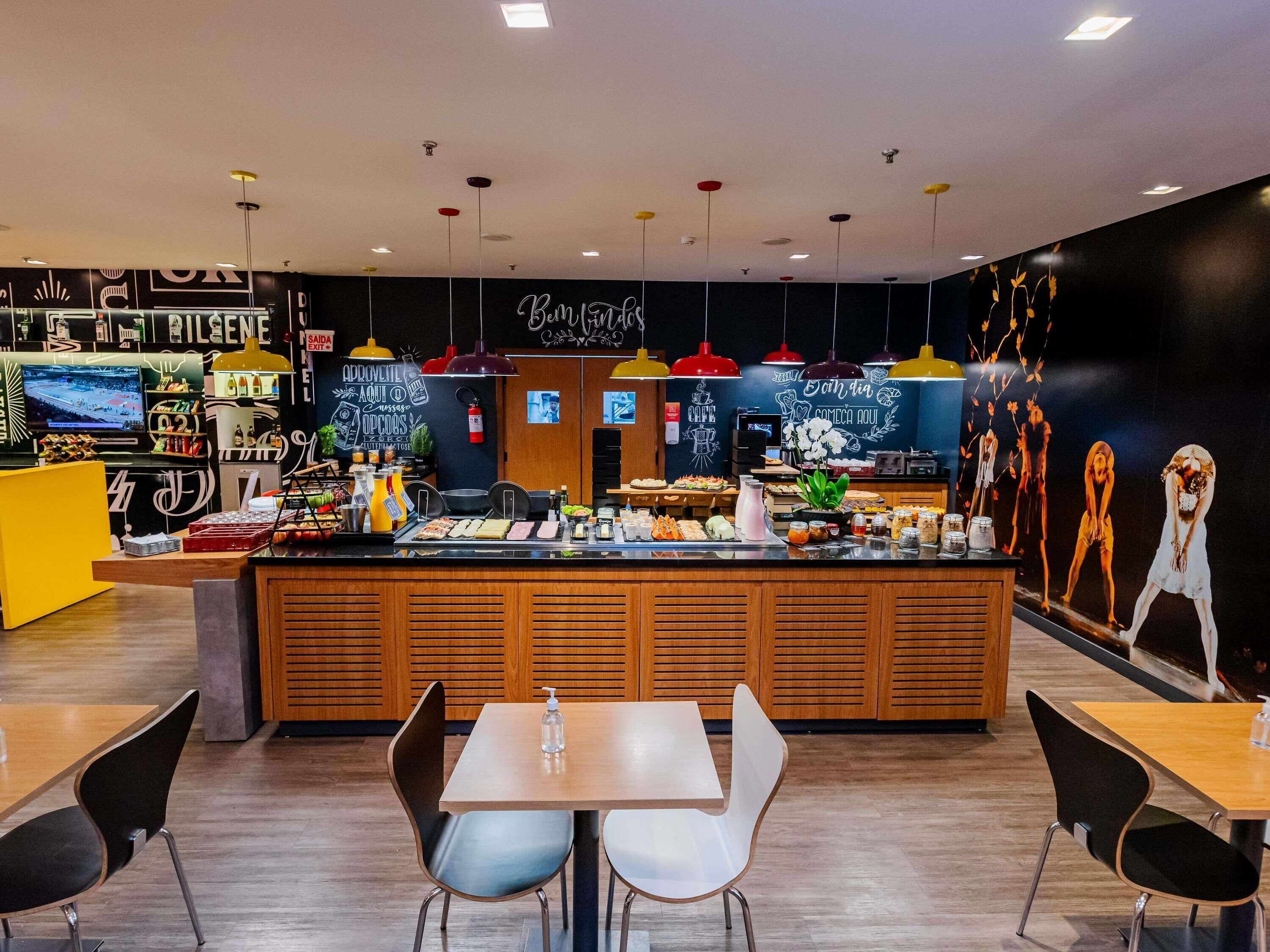 A cafe with a counter, tables, chairs, and a wall with artwork.