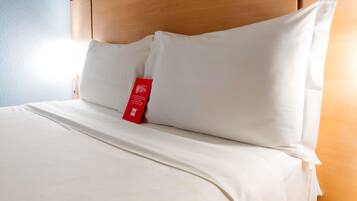 Una habitación de hotel con cabecera de madera, ropa de cama blanca y una etiqueta roja en la almohada.