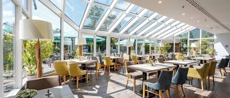 A spacious indoor area with tables and chairs, large windows, and a view of the outdoors.