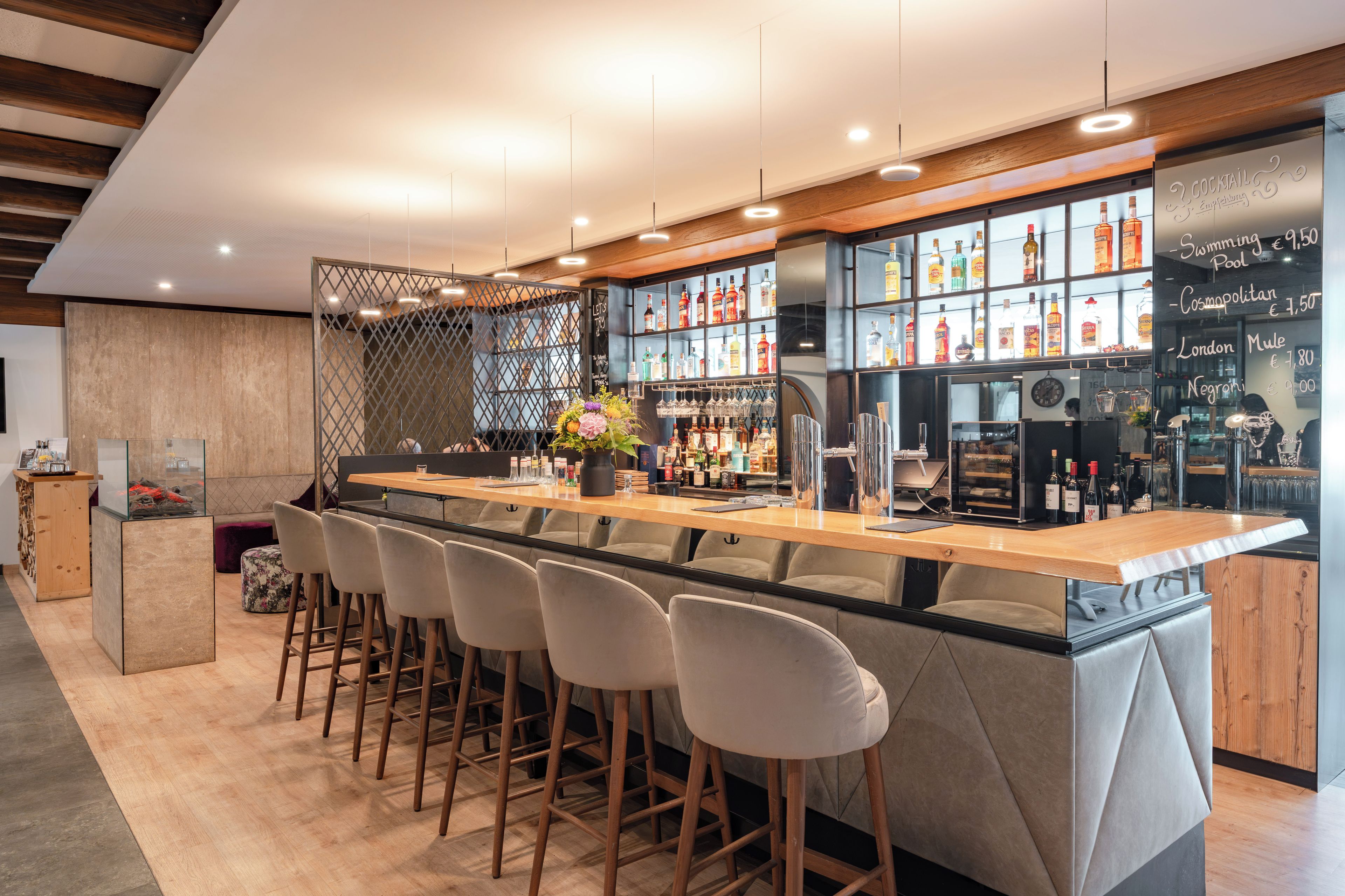 A modern bar area with a long counter, bar stools, and a variety of bottles and glasses.