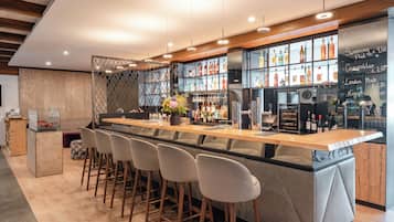 A modern bar area with a long counter, bar stools, and a variety of bottles and glasses.