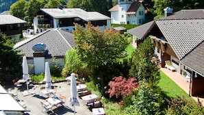 A chalet-style building with a steep roof, surrounded by lush greenery and a mountain backdrop. - HYPERION Hotel Garmisch – Partenkirchen (Garmisch-Partenkirchen)