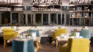 A restaurant with multiple dining tables and chairs, shelves with wine bottles, and a view through large windows. - HYPERION Hotel Garmisch – Partenkirchen (Garmisch-Partenkirchen)