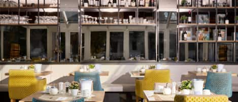 A restaurant with multiple dining tables and chairs, shelves with wine bottles, and a view through large windows.