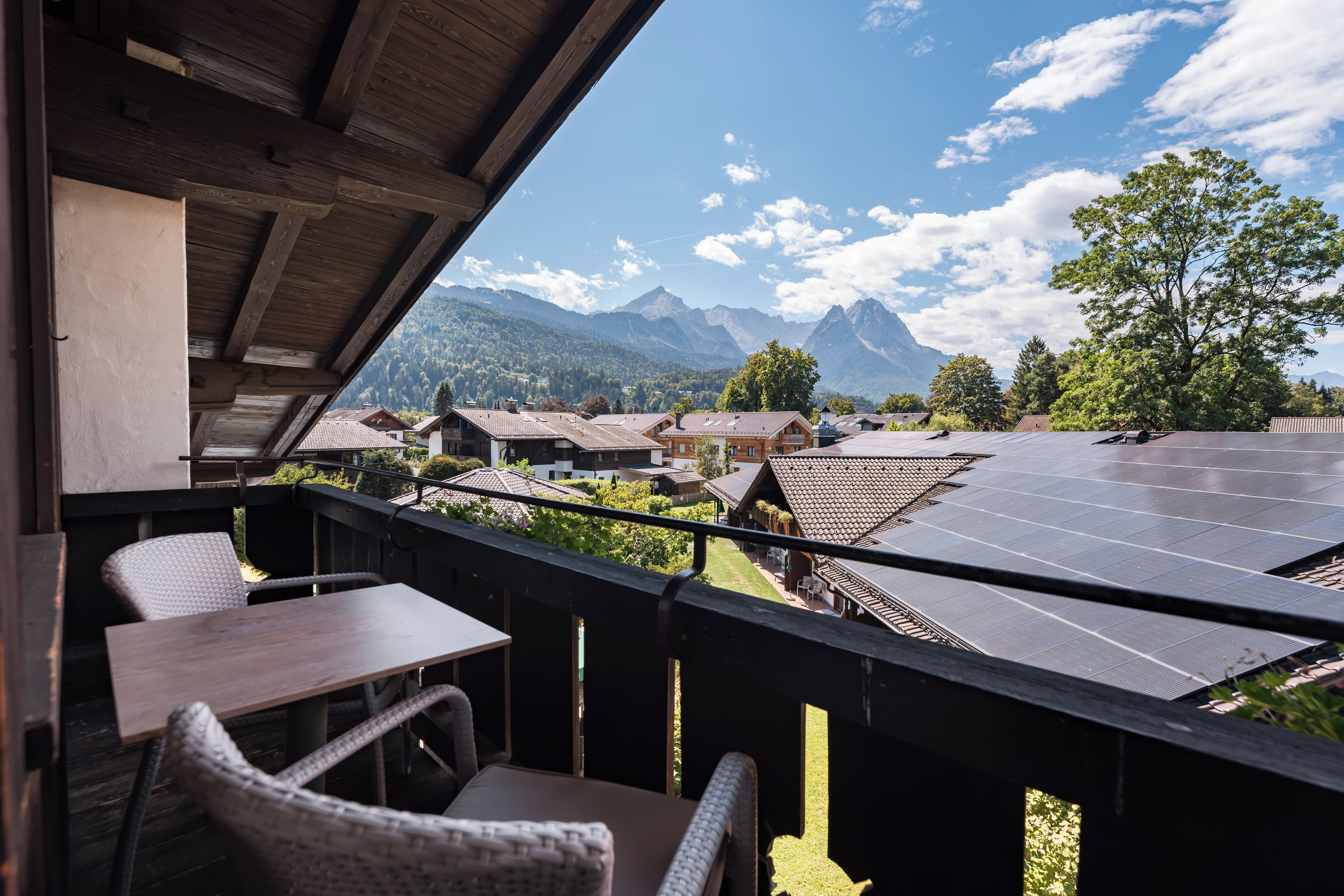 A balcony with a view of a mountain range, solar panels, and traditional buildings.