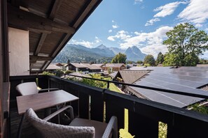 A balcony with a view of a mountain range, solar panels, and traditional buildings. - LA GAP Alpin Boutique Hotel (Garmisch-Partenkirchen)