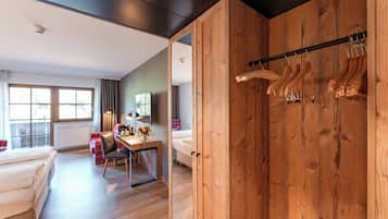 A modern hotel room with a wooden wardrobe, a dining area, a bed with a red and white checkered cover, and a window with curtains.