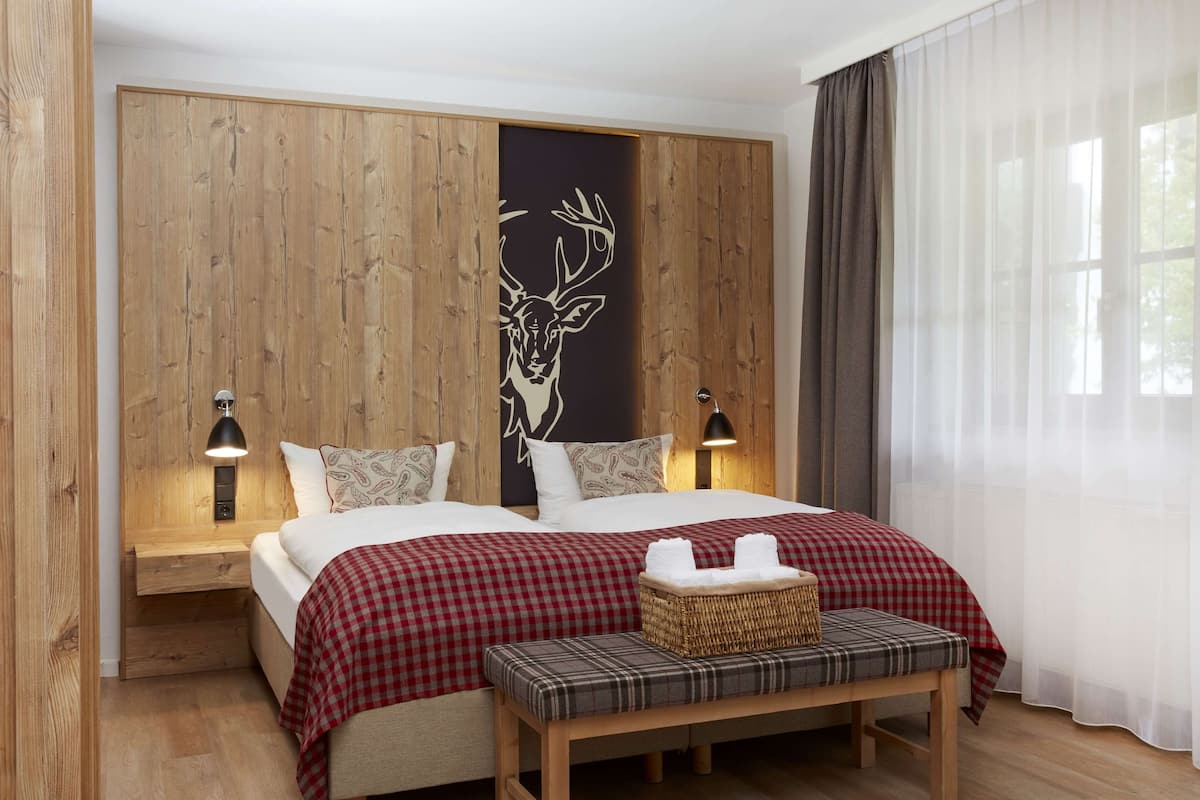 A bedroom with a wooden headboard, two beds, a bench, and a wall-mounted lamp.