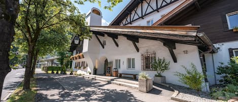 Een klassiek chalet met een schuin dak, een balkon met bloembakken en een stenen bank buiten.