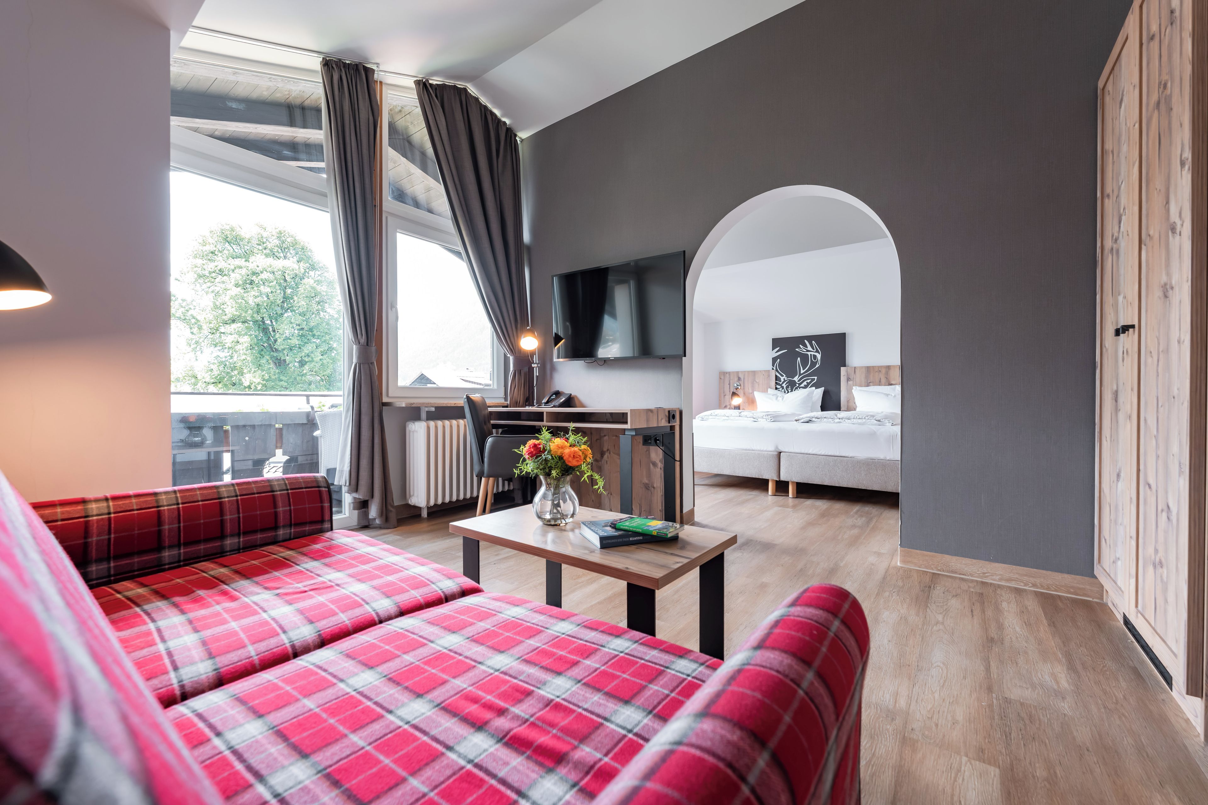 A modern room with a sofa, a small table with a vase, a bed, and a TV mounted on the wall.