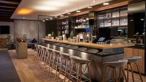 A modern bar area with a long counter, multiple stools, and a variety of glassware and bottles. - HYPERION Hotel Garmisch – Partenkirchen (Garmisch-Partenkirchen)