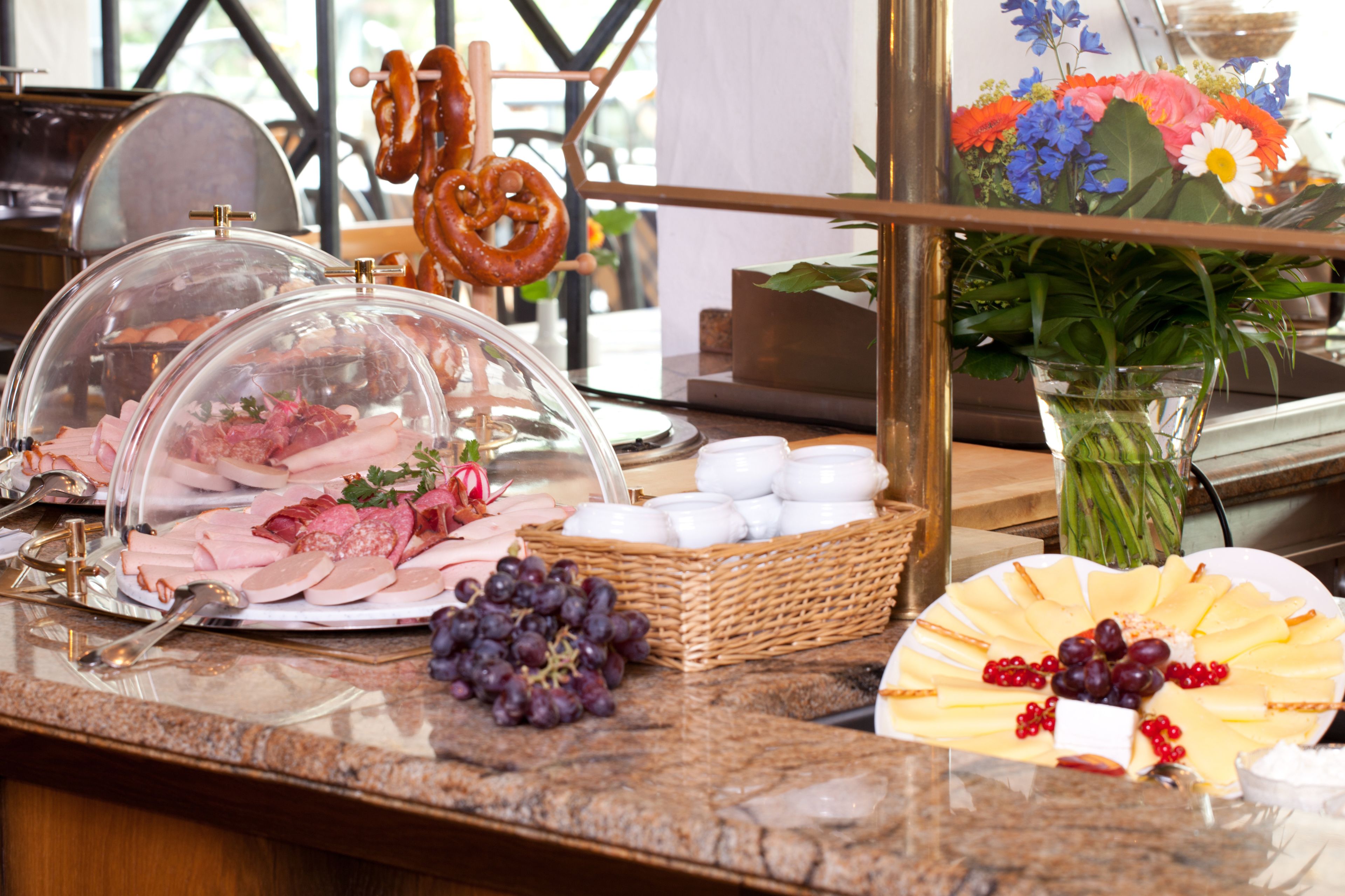 Un bufé con diversas opciones de comida, entre ellas carnes, quesos, uvas y un arreglo floral decorativo.