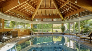 An indoor swimming pool with wooden beams, large windows, and lounge chairs. - HYPERION Hotel Garmisch – Partenkirchen (Garmisch-Partenkirchen)