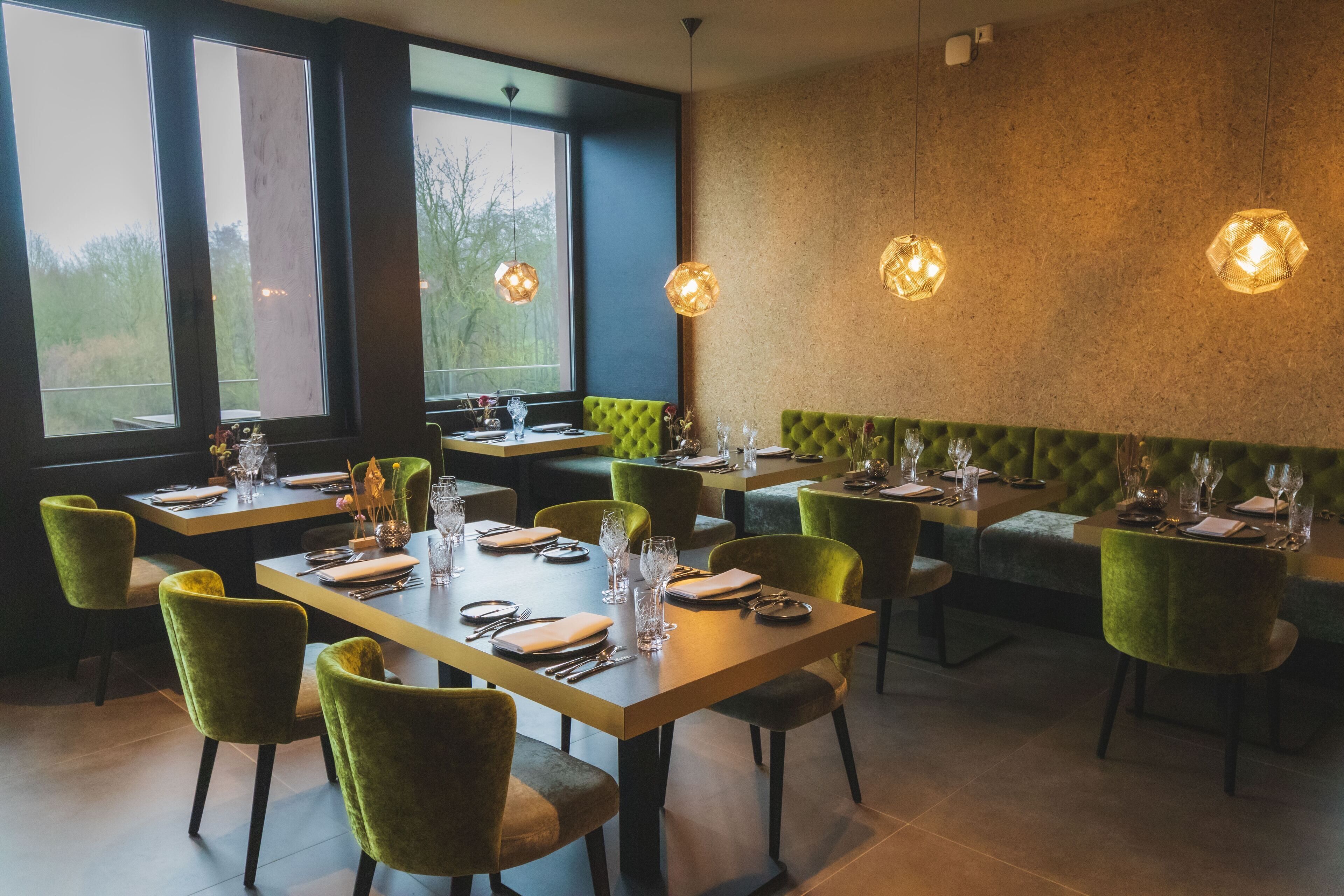 A restaurant with green upholstered chairs, wooden tables, and hexagonal pendant lights.