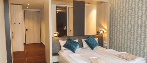 A modern hotel room with a large bed, two bedside tables, and a walk-in closet.