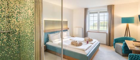 A hotel room with a large bed, a glass shower enclosure, a desk with a lamp, and a view of the outdoors.