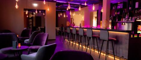 A bar area with purple lighting, bar stools, and a bar counter.
