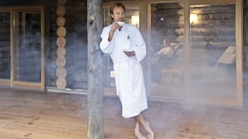 A person in a white robe standing in a wooden room with a large mirror and a wooden floor.