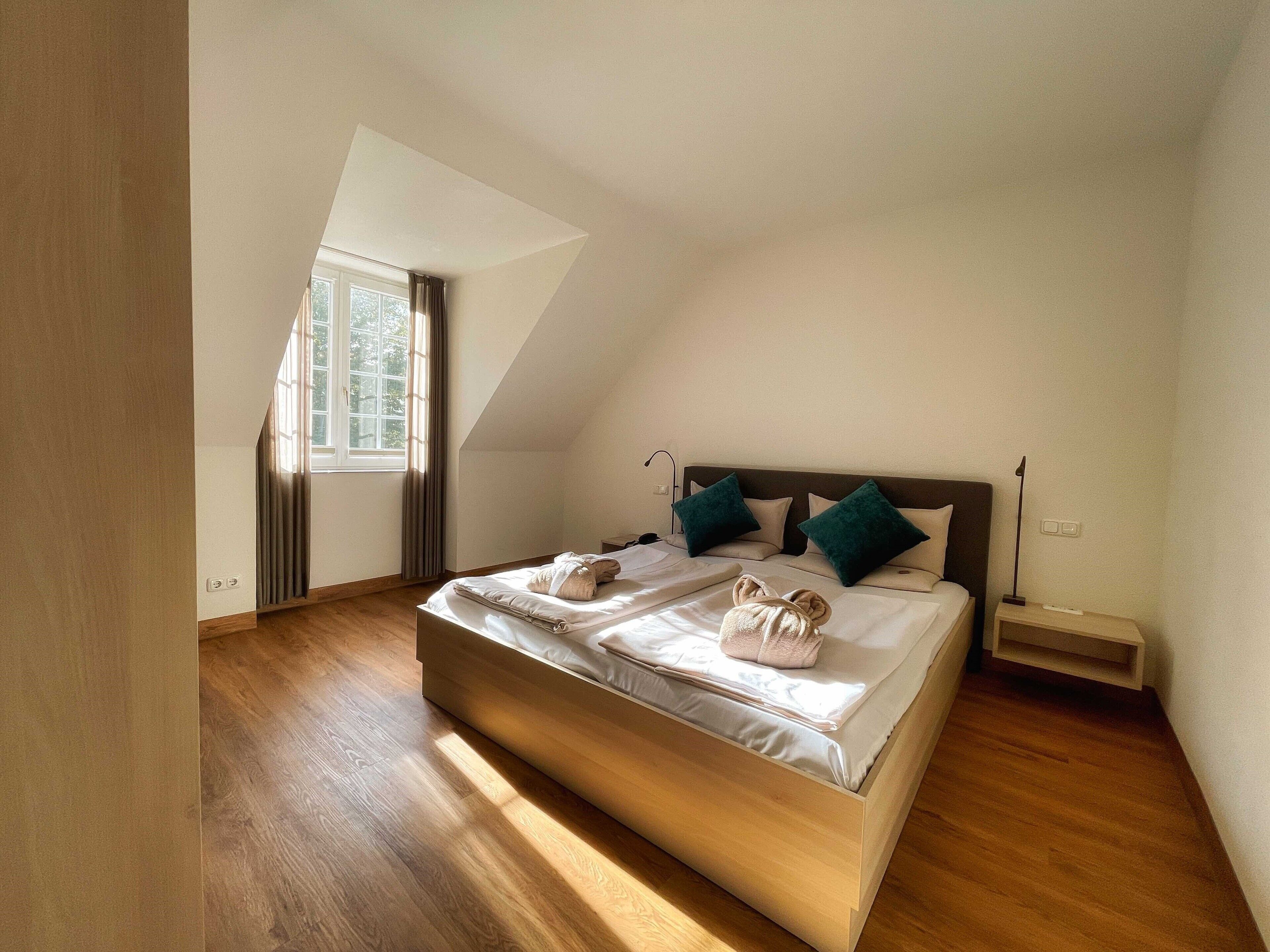 Een moderne slaapkamer met een schuine plafond, een groot bed met twee kussens en een nachtkastje.