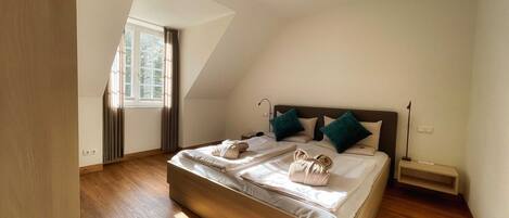 Een moderne slaapkamer met een schuine plafond, een groot bed met twee kussens en een nachtkastje.