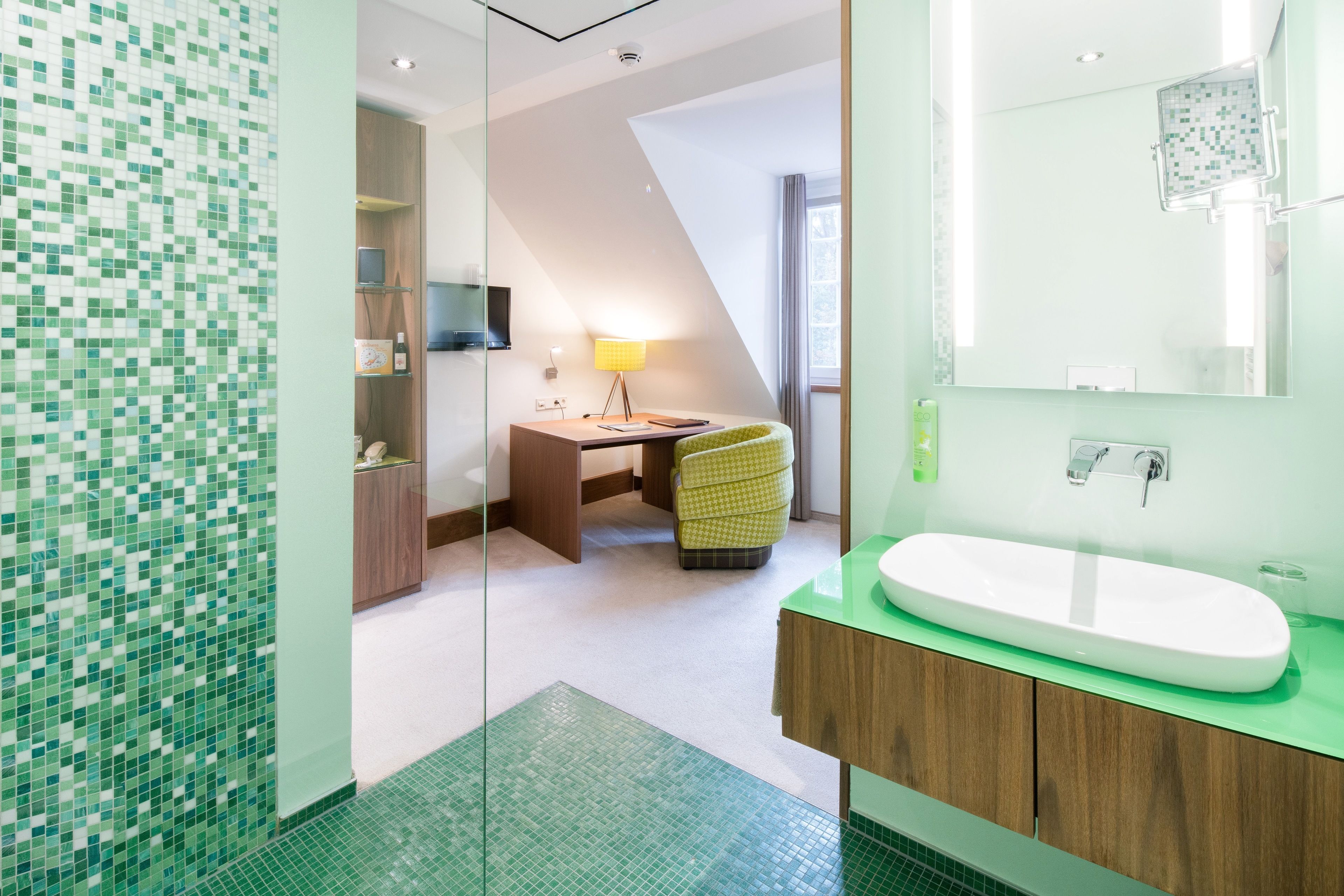 A modern bathroom with a green-tiled wall, a white sink, and a wooden vanity.