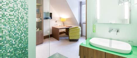 Un baño moderno con pared de azulejos verdes, un lavamanos blanco y un mueble de tocador de madera.
