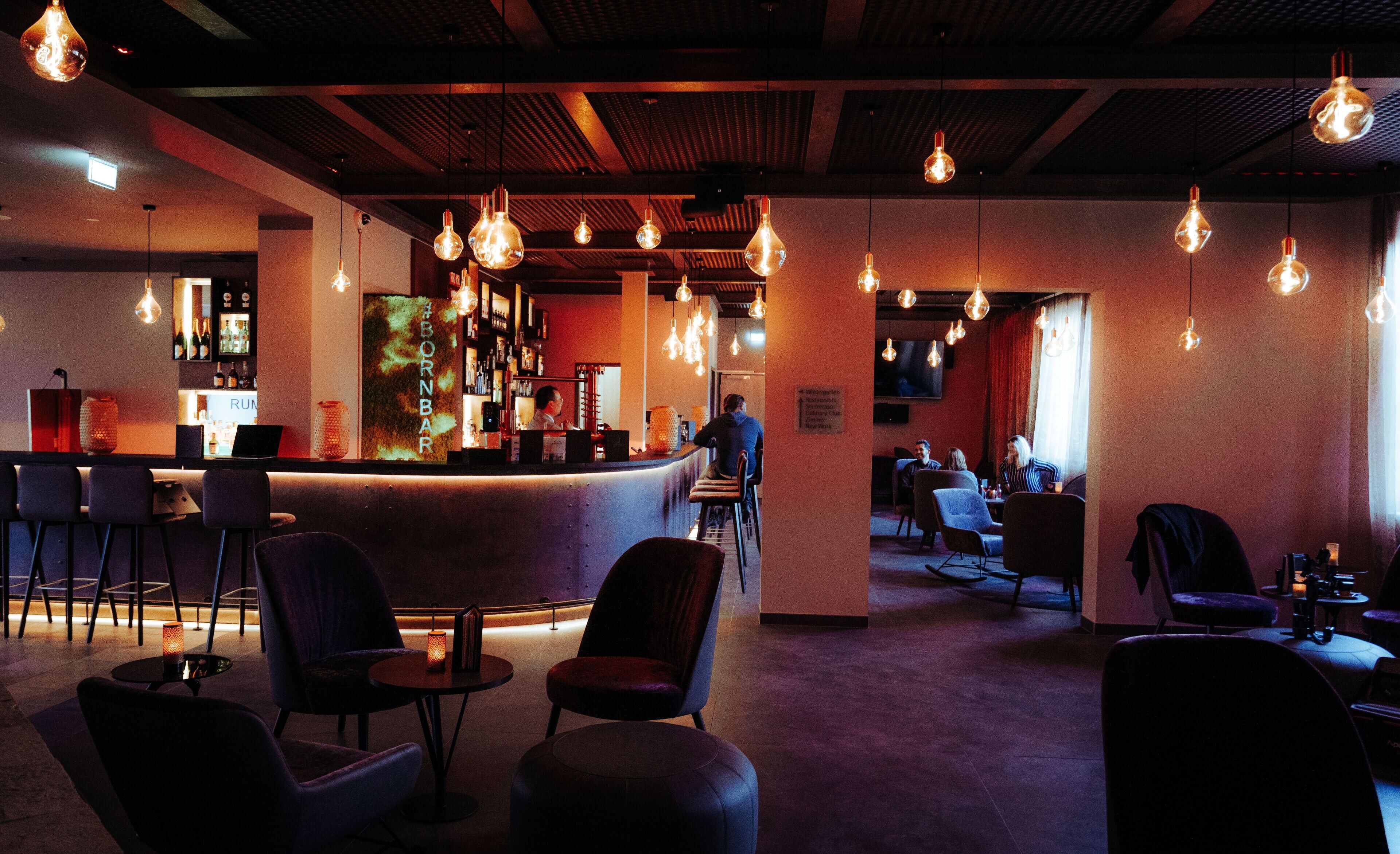 A bar area with hanging light bulbs, bar stools, and a counter.