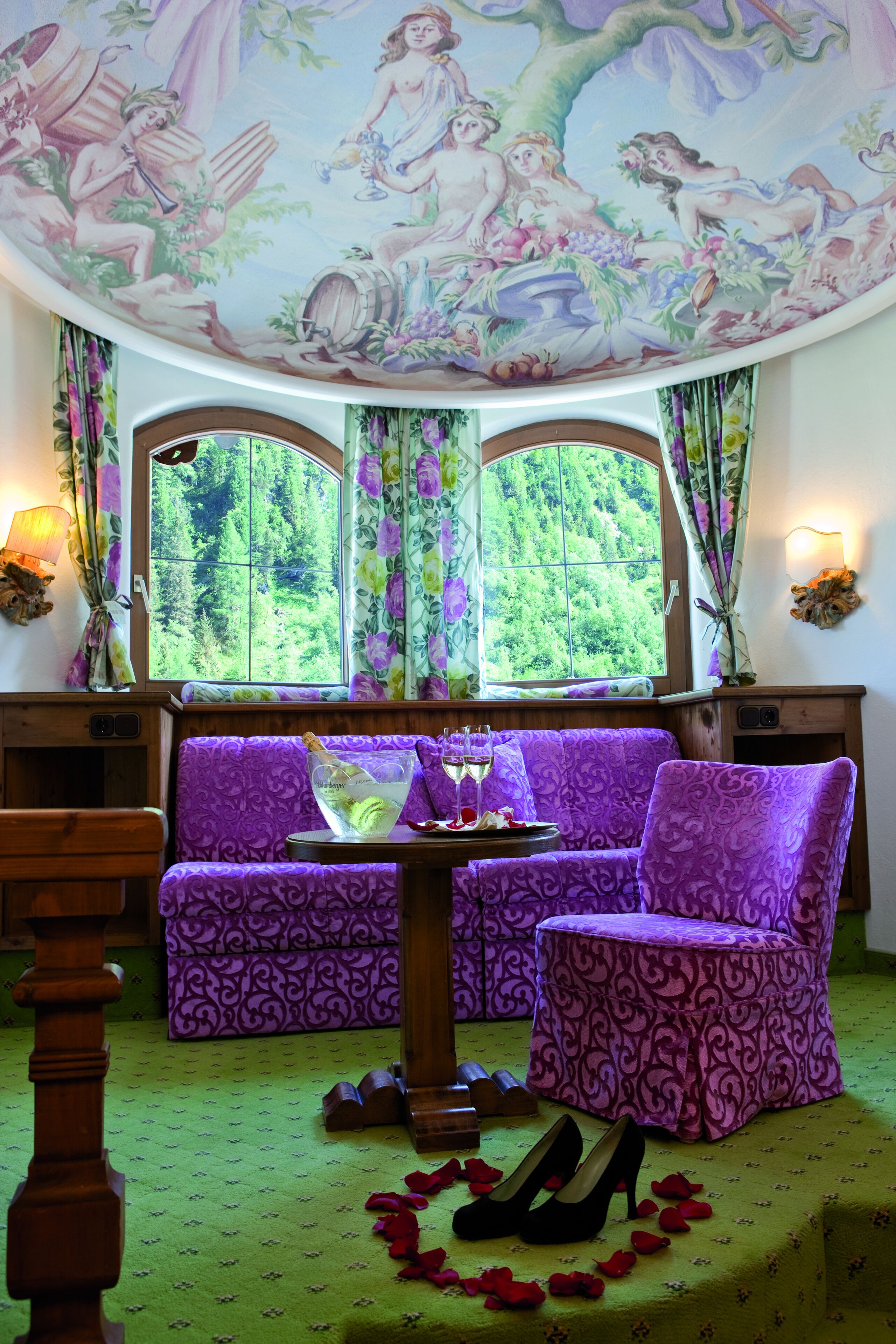 Ein Zimmer mit einem violetten Sofa und Sessel, einem Holztisch mit einem Glas sowie ein Paar Schuhe auf dem Boden.