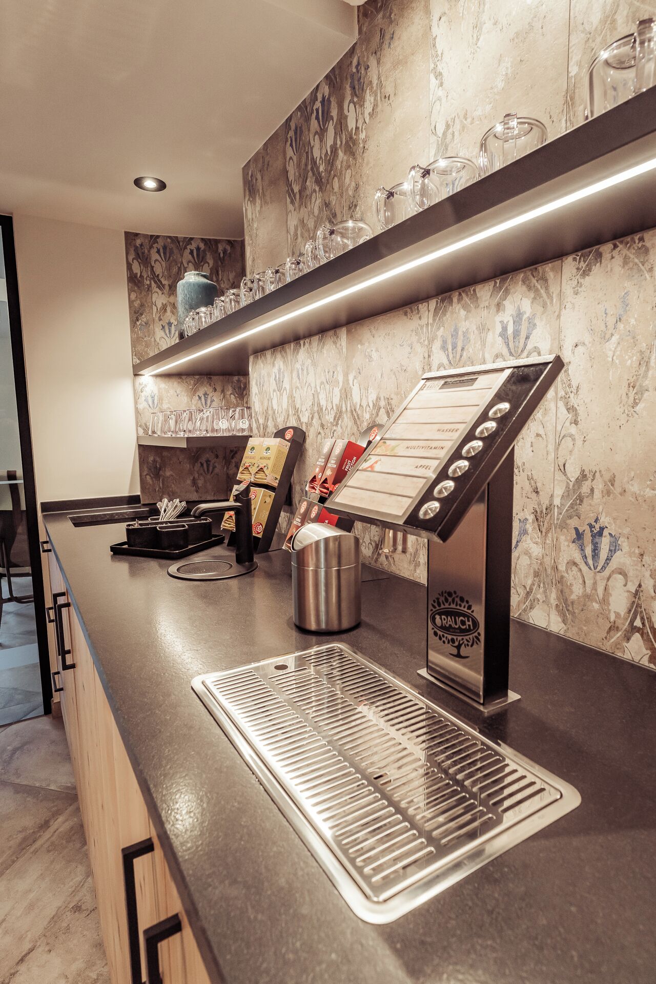 A modern bar area with a stainless steel counter, a coffee machine, and a menu stand.