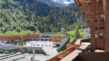 Vista da un balcone in legno su una zona montana con un edificio che include un centro sportivo e un parcheggio.
