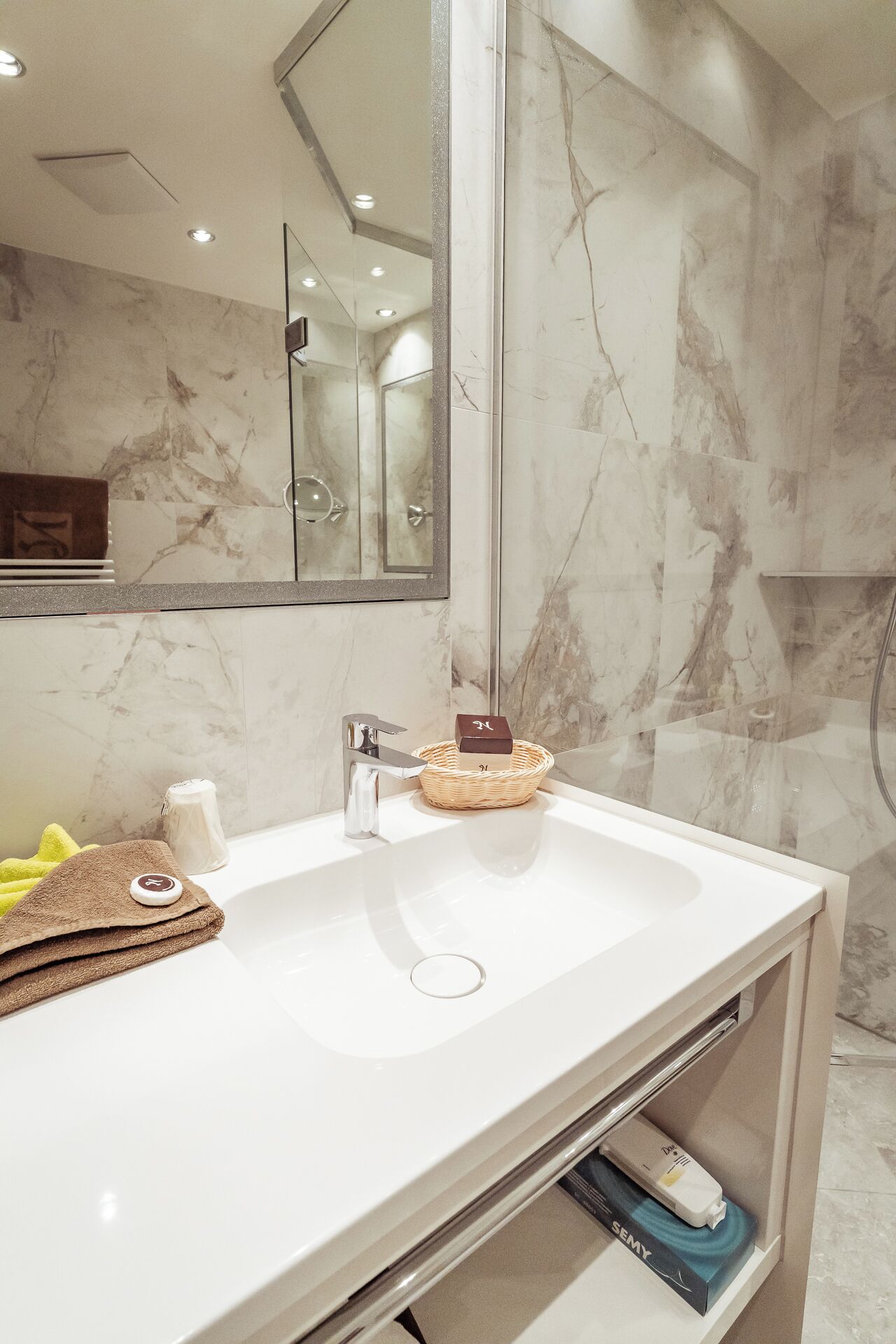 A modern bathroom with a white sink, a mirror, and a marble wall.