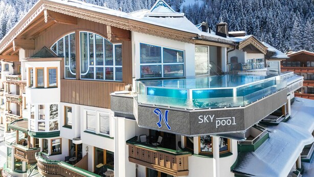 Et hotel med flere etager, en glasbalkon og en pool til skiløb.