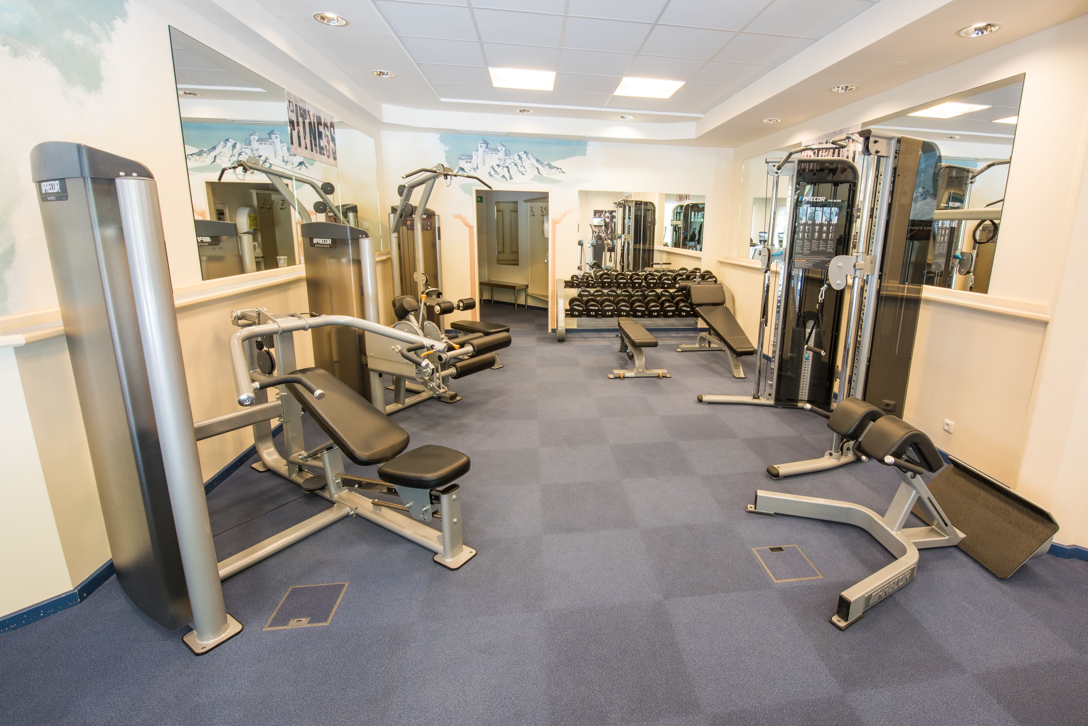 A gym with various exercise equipment, mirrors, and a blue carpet.