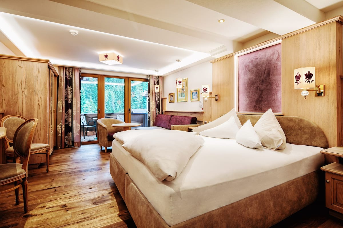 Habitación de hotel con una cama grande, suelo de madera, zona de comedor y vistas al exterior.