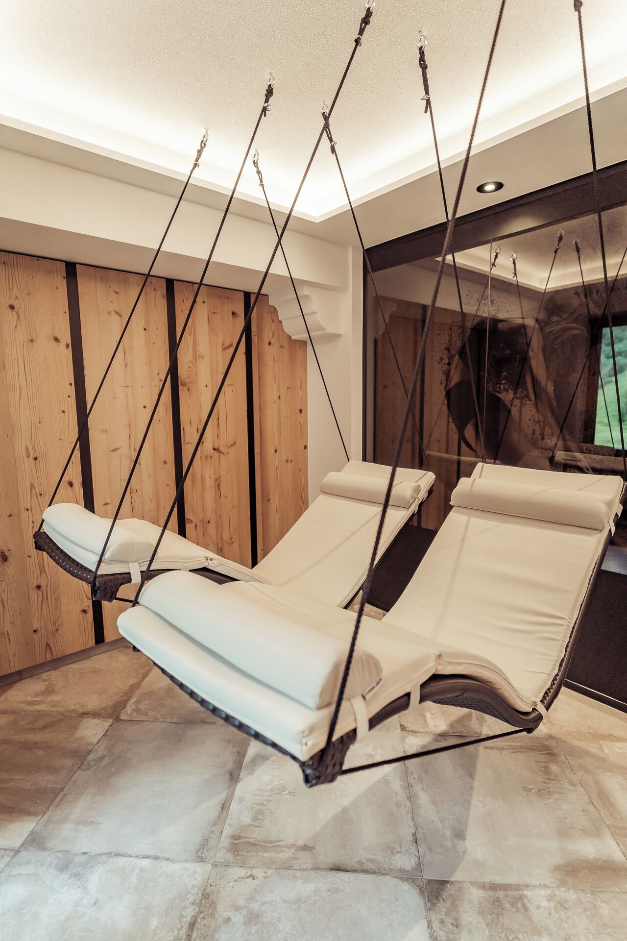 Una habitación con una silla de masaje colgante, paredes de madera y suelo de piedra.