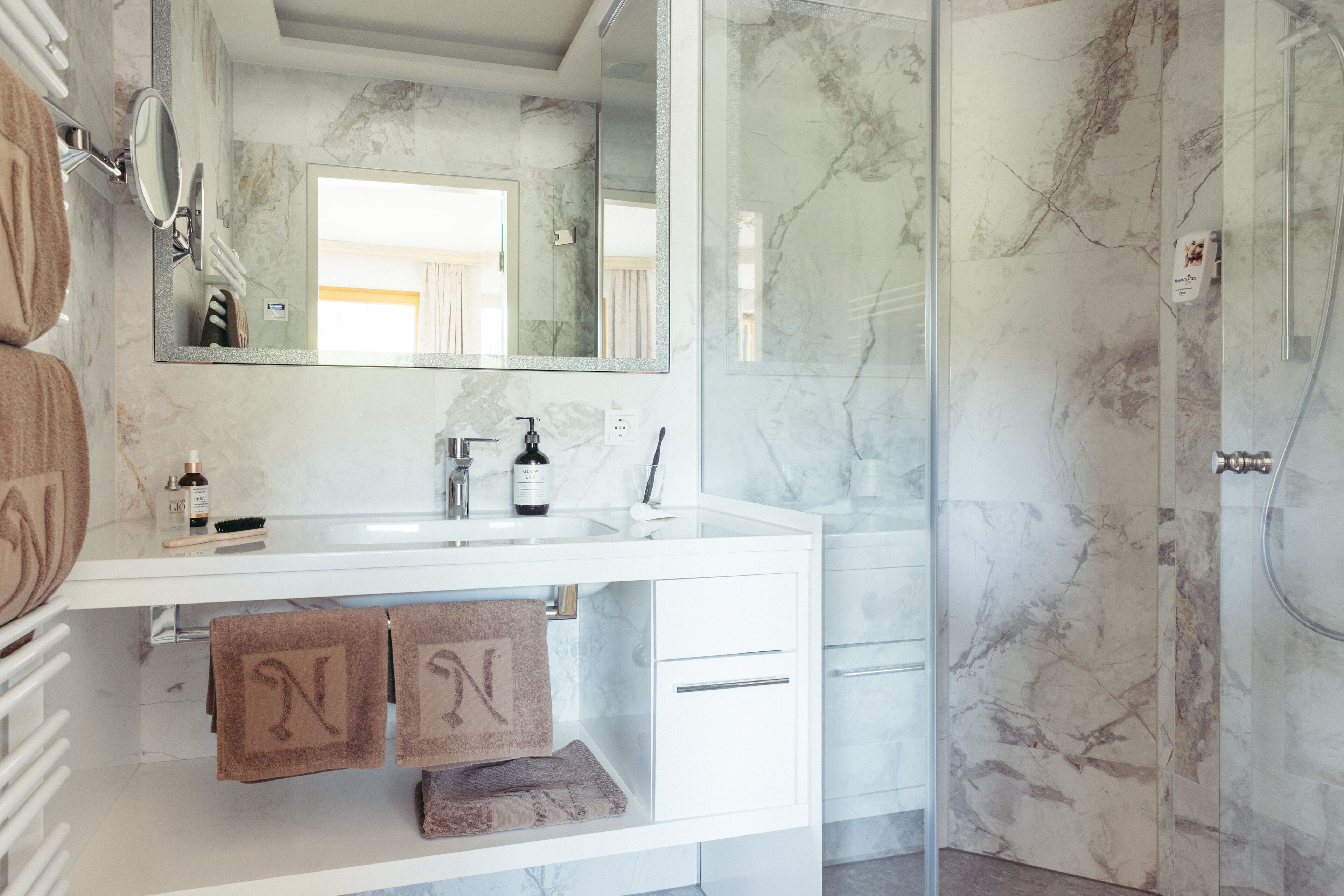 Une salle de bain moderne avec un lavabo en marbre, un grand miroir et une cabine de douche en verre.