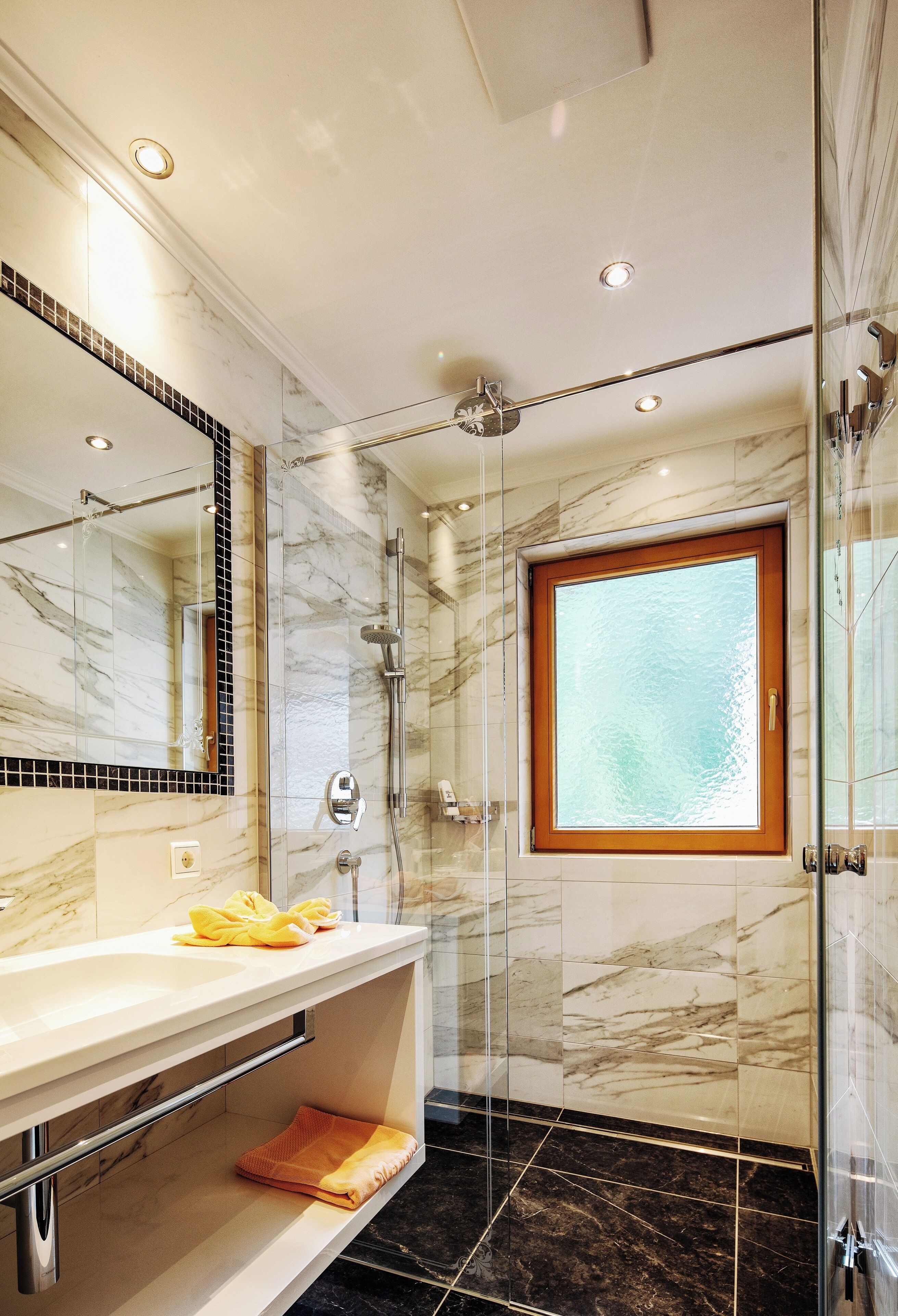 Un bagno moderno con doccia vetrata, parete in marmo e un ampio specchio, oltre a una finestra.