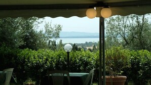 Un área de estar al aire libre con mesa y sillas bajo una pérgola, con vista a un lago y colinas.