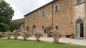Un edificio de piedra de dos pisos con un camino de grava y macetas con flores rosas al frente.