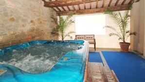 Un jacuzzi en una habitación con paredes de piedra, vigas de madera y plantas en macetas.