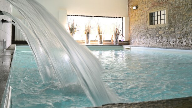 Una piscina interior con cascada, paredes de piedra y plantas en macetas.