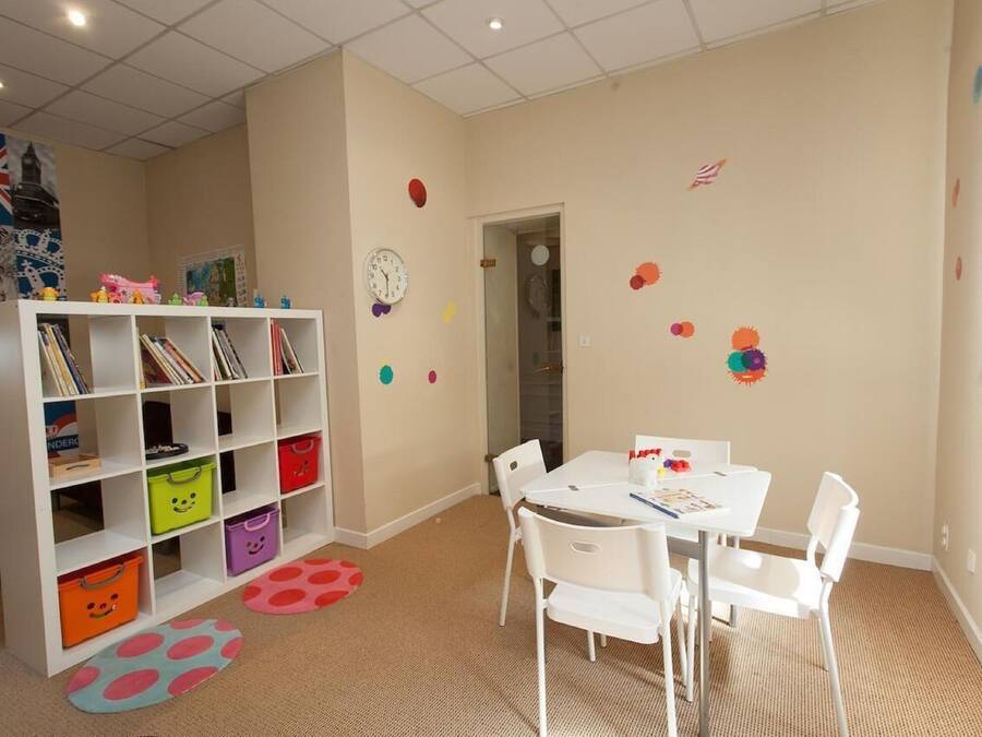 A room with a white bookshelf, a white table with chairs, and colorful storage bins.