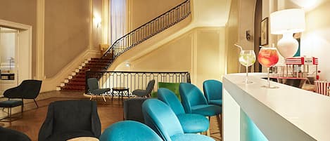Eine Lobby mit Treppe, blauen Stühlen, einer Bar und einem Chandelier.
