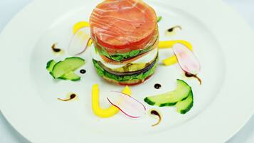 A white plate with a layered sandwich, cucumber slices, radish slices, and yellow sauce.