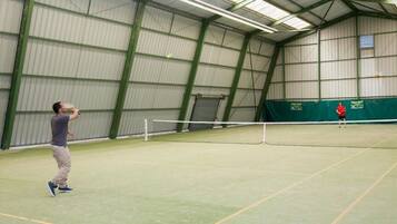 An indoor tennis court with a net, a player in the foreground, and another player in the background.