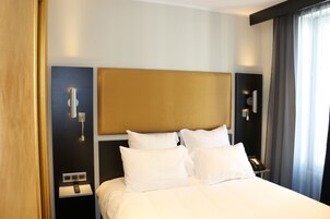 Una habitación de hotel con una cama grande, una mesita de noche con lámpara, un teléfono y una lámpara de pared.