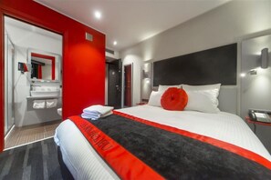 A modern hotel room with a large bed, a red accent wall, a bathroom with a mirror and sink, and a red and black bedspread. - Hôtel Boutique Richelieu Lyon Gare Part Dieu (Lyon)