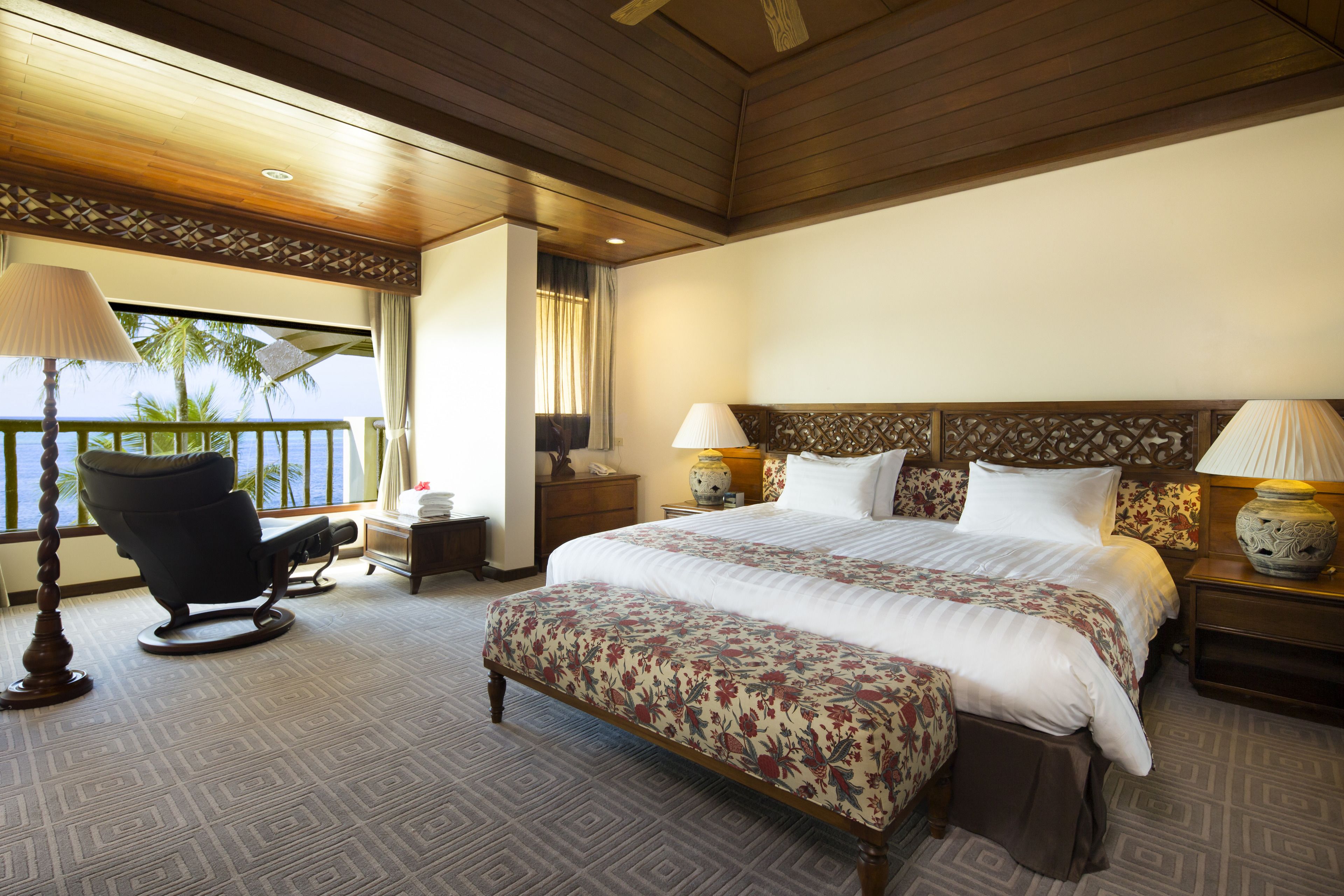 A hotel room with a large bed, two bedside tables with lamps, a chair, a desk, and a view of the ocean.