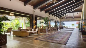 A spacious lobby with high ceilings, large windows, and a view of the ocean. There are multiple seating areas with sofas and chairs, and a large decorative rug on the floor. - Aqua Resort Club Saipan (Saipan)